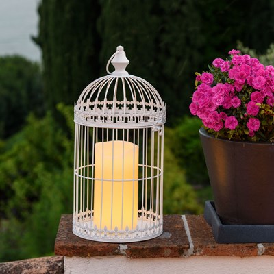 Lanterne blanche en forme de cage avec bougie pos&eacute;e sur un muret &agrave; c&ocirc;t&eacute; d'un pot de fleurs